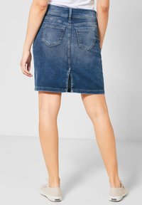 Jeanskjol i mörkblått, längre än knäna, med en öppning bak, två påsydda fickor och en figursydd midja. Avslappnad design med en slät textur.