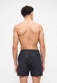Shorts de bain noirs en matériau léger, dotés d'une taille élastique et d'une poche arrière unique. Texture lisse et élégante.
