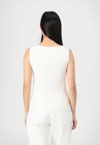 Top sans manches blanc à côtes avec un col rond, de forme ajustée et au design sans coutures ; porté avec un pantalon blanc taille haute.