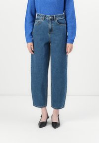 Jeans in denim blu a vita alta e dal fit comodo, con cinque tasche, lavaggio chiaro e orli sfilacciati, abbinati a scarpe nere con punta a punta.