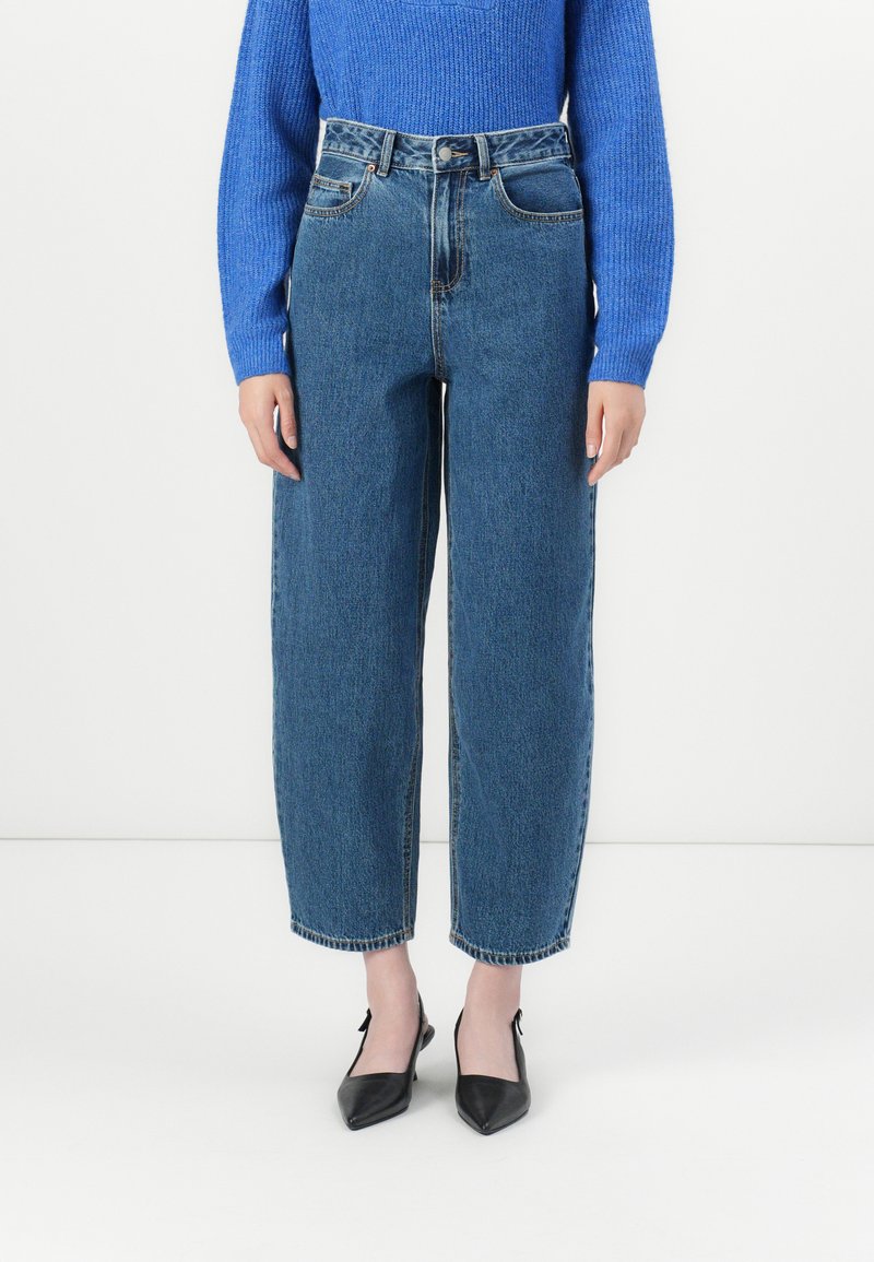 Jeans in denim blu a vita alta e dal fit comodo, con cinque tasche, lavaggio chiaro e orli sfilacciati, abbinati a scarpe nere con punta a punta.