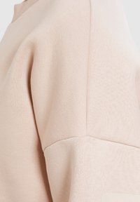 Sweatshirt rose clair avec une texture douce, doté d'un col rond, de détails de couture sur l'épaule et d'une coupe décontractée.