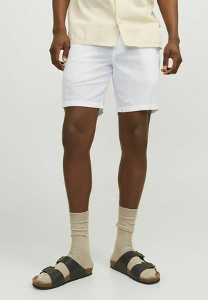 Witte linnen shorts met opgerolde manchetten, gecombineerd met zwarte en beige sandalen en beige kniehoge sokken. Focus op een casual zomerse stijl.