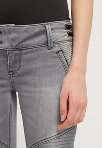 Pantalones de mezclilla gris con un diseño ajustado, con acentos acanalados laterales, detalles de cierre únicos y una textura suave.