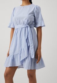 Gestreiftes blaues Kleid mit kurzen, gepufften Ärmeln, einem bindbaren Taillengürtel und einem ausgestellt geschnittenen Saum mit einem rüschierten Rand. Hergestellt aus leichtem Stoff.