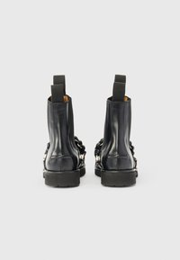 Μαύρες δερμάτινες μπότες μέχρι τον αστράγαλο με ελαστικές πλευρικές πάνες, επίπεδες λαστιχένιες σόλες και λεπτομέρειες με αλυσίδες στις πλευρές. Λείο υλικό και κλασικός σχεδιασμός.