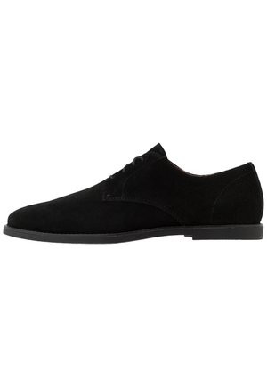 Chaussure habillée pour homme en daim noir avec fermeture à lacets et semelle plate basse, vue de profil sur fond blanc.