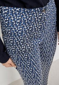 Pantalon bleu et blanc à motifs, en tissu texturé avec une coupe ajustée, doté d'une fermeture à boutons sur le devant et de poches.