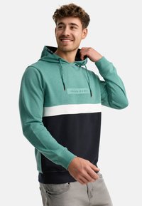 Felpa con cappuccio in blu teal, bianco e navy con design colorblock. Realizzata in un materiale morbido, presenta un patch con logo frontale e un cordoncino regolabile.
