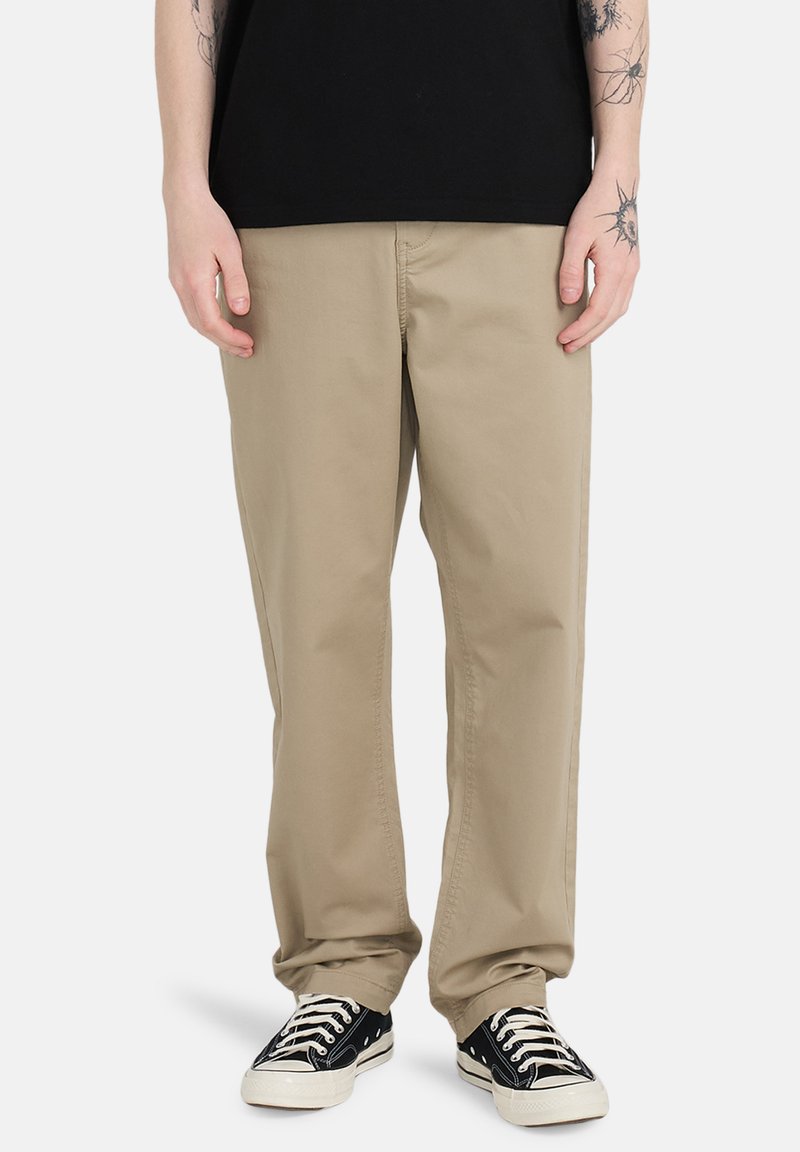 Beige bomuldsbukser med afslappet pasform, der har sidelommer og knaplukning, parret med sorte lavtoppede sneakers.