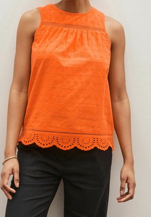 Haut sans manches orange vif avec broderie florale ajourée, ourlet festonné, porté avec un pantalon noir et un bracelet au poignet gauche.