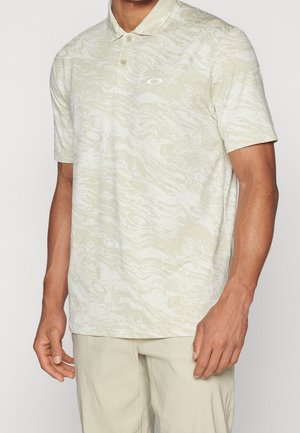 Homme portant un polo beige à manches courtes avec un motif ondulé subtil et un petit logo sur la poitrine, associé à un pantalon beige clair.