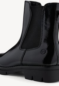 Stivaletto in pelle verniciata nera con pannelli laterali elastici e suola in gomma. Presenta dettagli di cucitura e un logo circolare vicino al tallone.