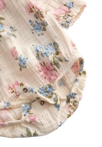 Body de algodón con estampado floral que presenta flores pink y azules sobre un fondo crema, con puños elásticos y cierres a presión en la parte inferior.