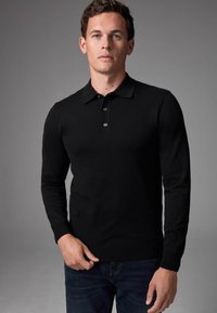 Sort langærmet polo sweater i slim fit, med en tre-knap lukning og ribbede manchetter, i en struktureret strikstof, båret med mørke jeans.