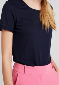 Camiseta de algodón azul marino con mangas cortas, escote redondo, combinada con pantalones rosa de tiro alto que presentan un delantero plano y trabillas para cinturón.