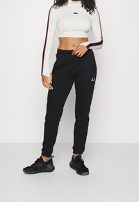 Los pantalones deportivos negros presentan una cintura con cordón y franjas laterales en rosa. La parte superior es de manga larga ajustada y corta en color crema con un detalle de logo.