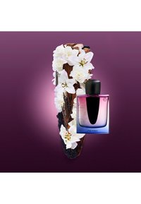 Shiseido-parfyme i en gradient glassflaske, med en svart kork. Omgitt av hvite blomster og mørke treakenter mot en lilla bakgrunn.