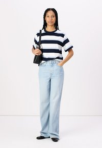Striped t-shirt in navy and white, paired with light blue wide-leg jeans. Accessories include a small black bag and black flats.