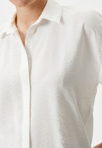 Witte blouse met korte mouwen en een knoopjesachtige kraag, gemaakt van een textuurstof en met een relaxte pasvorm, gericht op eenvoud en een minimalistisch ontwerp.