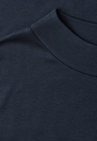 Gros plan d'un sweat-shirt bleu marine foncé à col rond montrant l'encolure repliée et la texture lisse du tissu en coton.