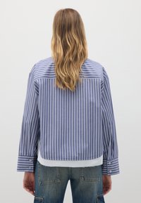 Camicia a righe blu e bianche con maniche lunghe, design corto e polsini con bottoni. Realizzata in un tessuto morbido e leggero.
