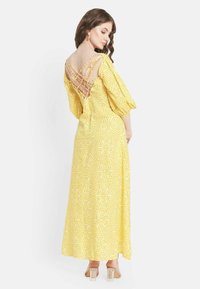 Gelbes Maxikleid mit Karomuster, Puffärmeln und Kreuzdetail im Rücken. Glatter Stoff mit fließendem Schnitt.