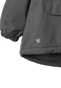 Harmaa eristetty takki, jossa on teksturoitu ulkopinta, joustavat hihansuut ja pehmeä fleecvuori sekä pieni logo helmassa.