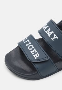 Sandalo scivoloso blu navy realizzato in materiale sintetico con due cinturini regolabili che presentano il testo del marchio bianco. Suola nera testurizzata per una migliore aderenza.