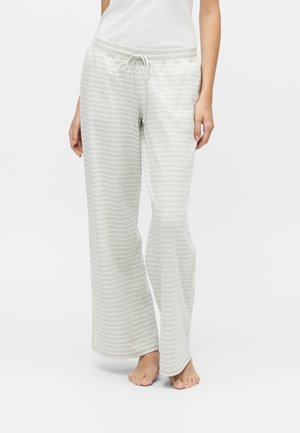 Femme portant un pantalon large rayé gris clair et blanc avec une taille à cordon, debout pieds nus sur un sol blanc.