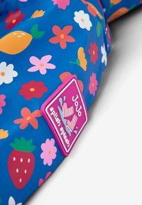 Vibrantna vodootporna tkanina u plavoj boji s živopisnim cvijećem i voćem, s ružičastim logom "JoJo Splish Splash". Glatka tekstura.
