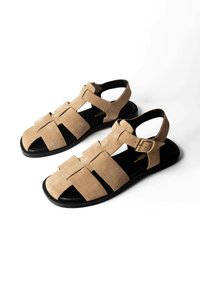 Sandales pêcheur en daim beige avec semelles noires et brides latérales à boucle, conçues pour un usage décontracté.