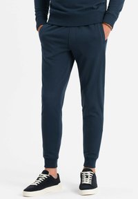 Pantalones jogger en color navy, confeccionados en material suave, con cinturilla elástica, bolsillos laterales y puños acanalados, combinados con zapatillas negras.