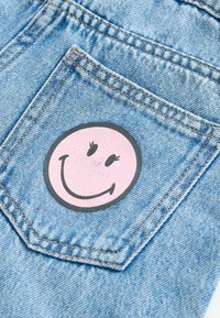 Visage souriant rose avec des cils imprimé sur la poche arrière d'un jean en denim bleu clair.