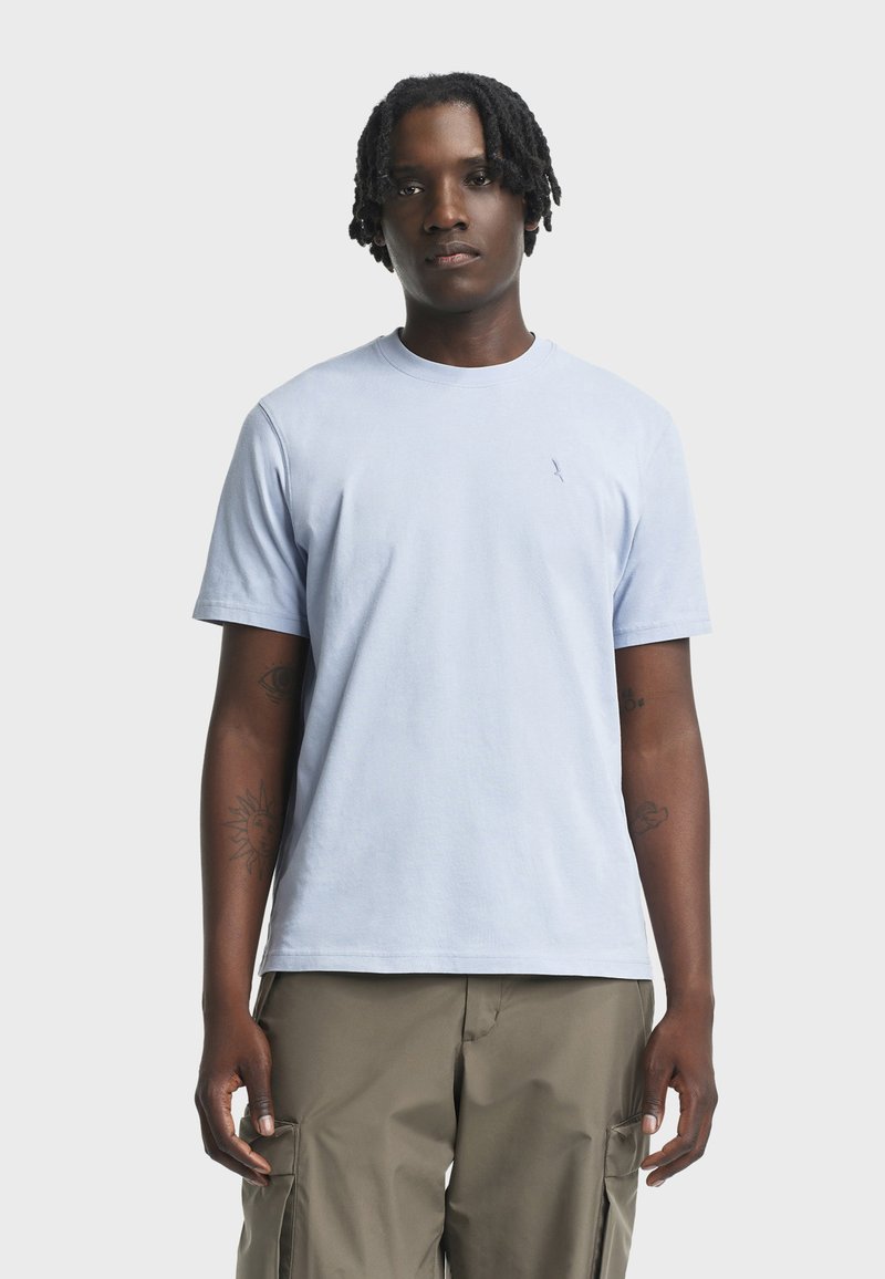 T-shirt di cotone azzurro chiaro con colletto tondo e maniche corte. Presenta un piccolo logo sul petto. Abbinato a pantaloni cargo beige larghi.