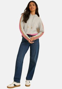 Sudadera gris cortada con rayas rosas y marrones en las mangas, combinada con jeans oscuros de cintura alta y zapatillas blancas con detalles negros.