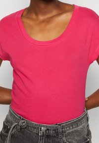 Tætsiddende kortærmet T-shirt i lys pink, med en bred bådudskæring og blødt, glat bomuldsstof. Sammen med høj talje grå jeans.