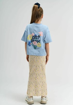 Hele sinine puuvillane t-särk, millel on lilleline graafika ja tekst "C'est la vie", koos kreemja ribaga seeliku ning mitmevärviliste lillemusteritega.