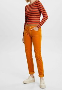 Pantalon en velours côtelé orange à coupe slim, avec un design à cinq poches et un ourlet retroussé. Assorti d'un haut à manches longues rouge à rayures.