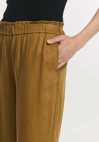 Tan, lichtgewicht broeken met een elastische tailleband en zijzakken. De stof heeft een gladde textuur en een losse pasvorm.