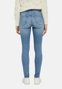 Jeans skinny de mezclilla azul con cintura de altura media, que presentan dos bolsillos traseros y un diseño de pierna ajustada. Combinados con un suéter de punto color crema.