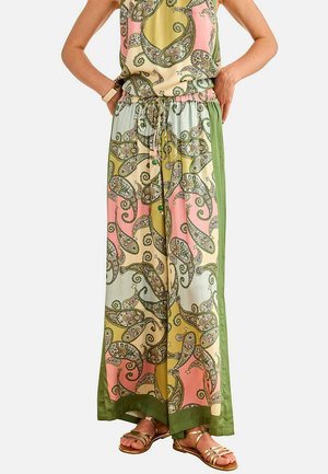 Mujer vistiendo pantalones de pierna ancha con estampado de cachemira en tonos pastel y franjas laterales verdes, combinados con sandalias doradas de tiras.