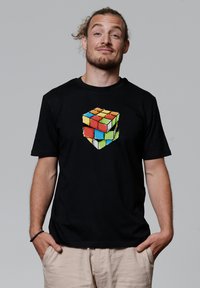 Zwarte t-shirt met een pixelachtige Rubik's Cube grafiek in levendige kleuren (rood, blauw, groen, geel) gecentreerd aan de voorkant. Korte mouwen.