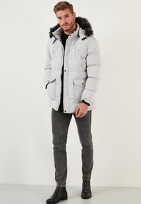 Pelēks pufīgs ziemas žakets ar ādas apdari, aprīkots ar pūkainu kapuci, priekšējām kabatām, rāvējslēdzēju un elegantu dizainu. Valkā ar pelēkiem džinsiem un melnām zābakām.