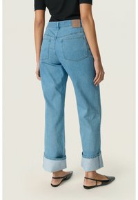 Jeans de mezclilla azul claro con un corte relajado, puños doblados, bolsillos traseros visibles y una etiqueta rectangular de cuero en la cintura.