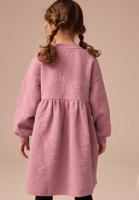 Lyserød, langærmet kjole lavet af tekstureret stof med sløjfemønster; indsnævret talje; rund halsudskæring; egnet til børn.