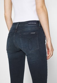 Jeans in denim blu scuro con un design aderente, dotati di un'etichetta Calvin Klein sul retro e dettagli di cucitura distintivi nelle tasche.