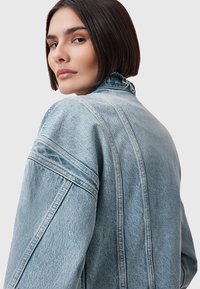 Chaqueta de mezclilla color azul claro con un cuello desgastado, ajuste oversize y detalles de costura prominentes. La vista muestra la parte posterior y el área del hombro.