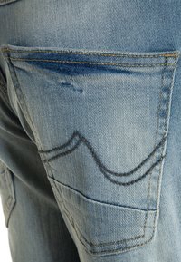 Pantalones vaqueros de mezclilla de color azul claro con un diseño de bolsillos traseros curvados, costuras en contraste y un acabado de tela suave y texturizado.