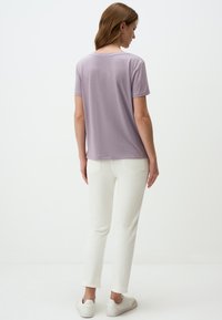 T-shirt lilla a maniche corte con una vestibilità comoda, abbinato a jeans white slim-fit e sneakers bianchi, che mostrano una superficie liscia e un design casual.